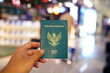 © Daniel Pawer - Asian man's hand holding a passport at the airport with people passing by in the background.