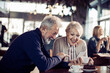 © Davor - Smiling senior couple using smartphone at cafe