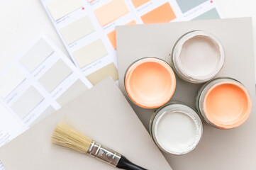 Tiny sample paint cans during house renovation, process of choosing paint for the walls, Peach Fuzz color of the year 2024, color charts on background