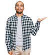 © Krakenimages.com - Hispanic adult man wearing casual clothes smiling cheerful presenting and pointing with palm of hand looking at the camera.