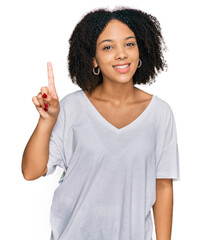 Wall Mural - Young african american girl wearing casual clothes showing and pointing up with finger number one while smiling confident and happy.