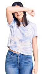 Young beautiful girl wearing casual t shirt covering eyes with arm smiling cheerful and funny. blind concept.