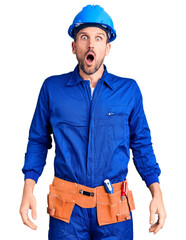 Canvas Print - Young handsome man wearing worker uniform and hardhat afraid and shocked, surprise and amazed expression with hands on face