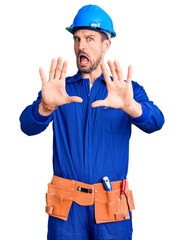 Wall Mural - Young handsome man wearing worker uniform and hardhat shouting frustrated with rage, hands trying to strangle, yelling mad