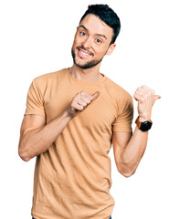 Canvas Print - Hispanic man with beard wearing casual t shirt pointing to the back behind with hand and thumbs up, smiling confident