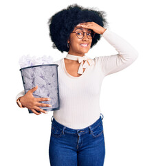 Poster - Young african american girl holding paper bin full of crumpled papers stressed and frustrated with hand on head, surprised and angry face