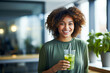 A beautiful African American woman is smiling and drinking a detox cocktail at home in the kitchen