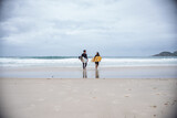 Fototapeta Konie - Couple of surfers walking along the beach with their boards under their arms, talking.