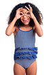 African american child with curly hair wearing swimwear doing ok gesture like binoculars sticking tongue out, eyes looking through fingers. crazy expression.