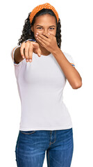 Wall Mural - Young african american girl wearing casual clothes laughing at you, pointing finger to the camera with hand over mouth, shame expression