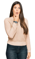 Poster - Young brunette woman wearing casual winter sweater looking fascinated with disbelief, surprise and amazed expression with hands on chin