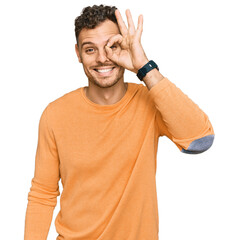 Wall Mural - Young hispanic man wearing casual clothes doing ok gesture with hand smiling, eye looking through fingers with happy face.