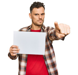 Canvas Print - Young hispanic man holding blank empty banner pointing with finger to the camera and to you, confident gesture looking serious