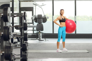 Poster - Young sporty female standing with an exercise ball at a fitness center