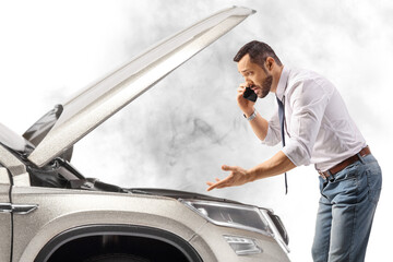 Wall Mural - Stressed young man with a car looking under the hood and talking on the phone