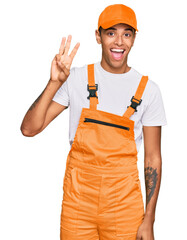 Canvas Print - Young handsome african american man wearing handyman uniform showing and pointing up with fingers number three while smiling confident and happy.