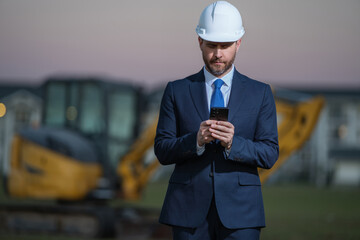 Wall Mural - Construction owner near excavator. Confident construction owner in front of house. Architect, civil engineer. Man construction owner with a safety vest and hardhat at construction site.