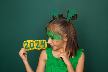 A happy attractive laughing girl with mask holds the numbers of the 2024 new year. Headdress in the shape of dragon wings