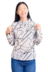 Wall Mural - Young beautiful chinese woman wearing casual shirt very happy and excited doing winner gesture with arms raised, smiling and screaming for success. celebration concept.