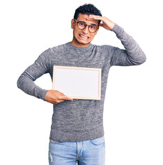 Sticker - Hispanic handsome young man holding blank empty banner stressed and frustrated with hand on head, surprised and angry face