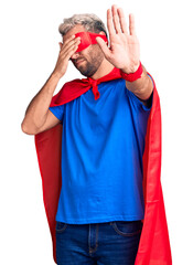 Poster - Young blond man wearing super hero custome covering eyes with hands and doing stop gesture with sad and fear expression. embarrassed and negative concept.