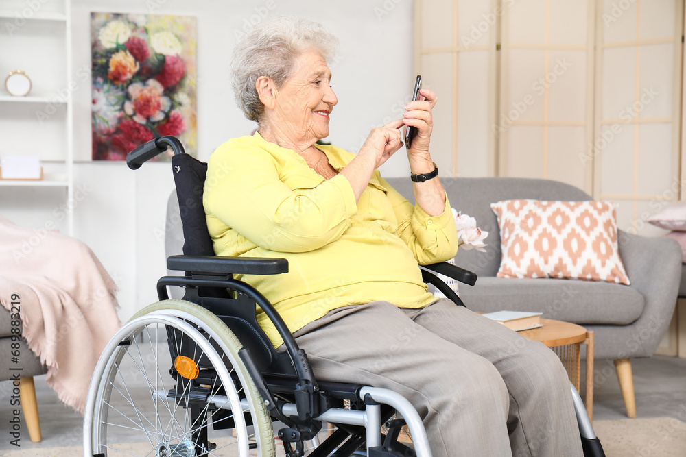 Senior woman in wheelchair using mobile phone at home