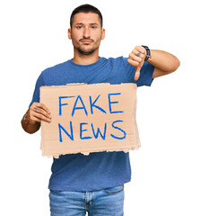 Canvas Print - Handsome man with tattoos holding fake news banner with angry face, negative sign showing dislike with thumbs down, rejection concept