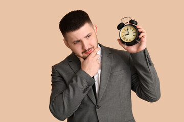 Young thoughtful businessman with alarm clock on beige background. Time management concept