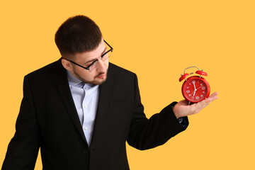 Young shocked businessman with alarm clock on yellow background. Time management concept