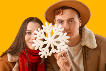 Wall Mural - Young couple in winter clothes with snowflake on yellow background, closeup