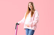 Beautiful young pregnant woman with electric kick scooter on pink background