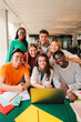© Jose Calsina - Vertical portrait. Group of young teenage students siting at library, using a laptop and looking at camera. Happy classmates studying and doing homeworks at high school. Multiracial academy people