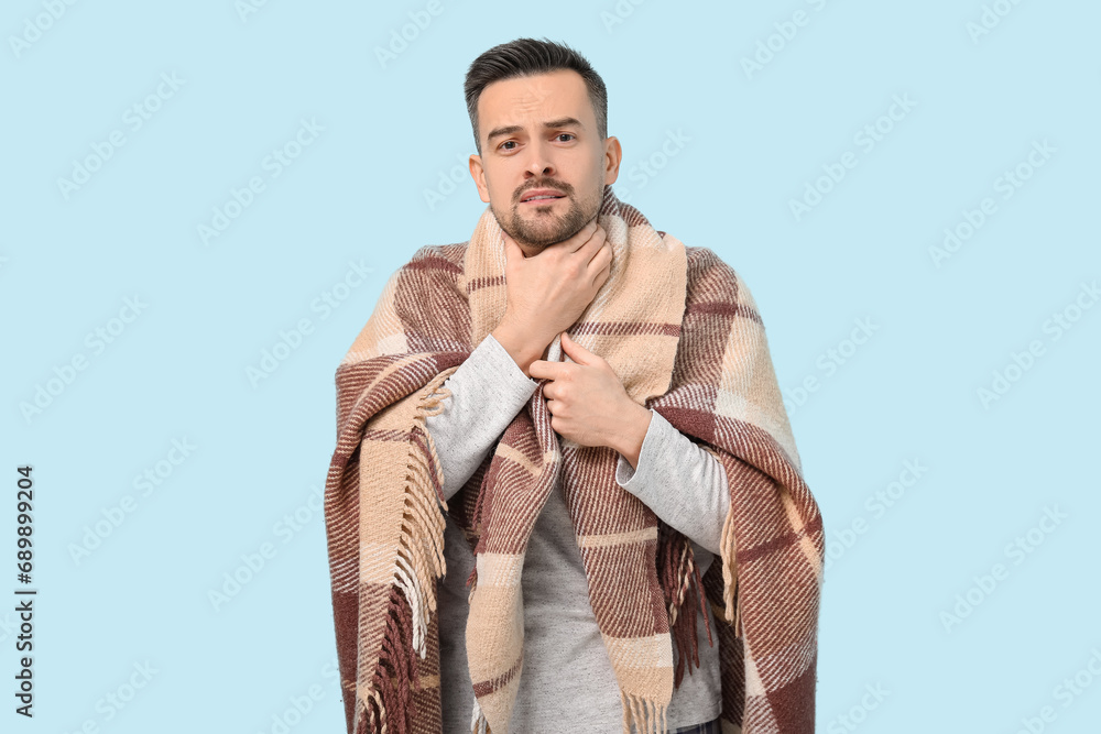 Sick young man with plaid on blue background