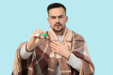 Poster - Sick young man with plaid and thermometer on blue background, closeup