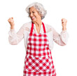 © Krakenimages.com - Senior grey-haired woman wearing apron very happy and excited doing winner gesture with arms raised, smiling and screaming for success. celebration concept.