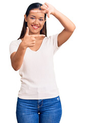 Sticker - Young beautiful latin girl wearing casual white t shirt smiling making frame with hands and fingers with happy face. creativity and photography concept.