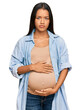 © Krakenimages.com - Beautiful hispanic woman expecting a baby showing pregnant belly with serious expression on face. simple and natural looking at the camera.