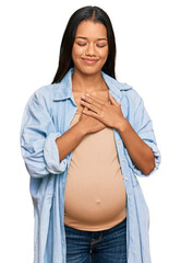 Sticker - Beautiful hispanic woman expecting a baby showing pregnant belly smiling with hands on chest with closed eyes and grateful gesture on face. health concept.