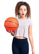 © Krakenimages.com - Beautiful kid girl with curly hair holding basketball ball scared and amazed with open mouth for surprise, disbelief face
