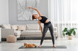 © New Africa - Beautiful woman with cute red cat practicing yoga on mat at home