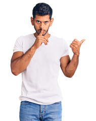 Sticker - Young latin man wearing casual clothes asking to be quiet with finger on lips pointing with hand to the side. silence and secret concept.