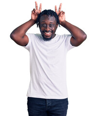 Poster - Young african american man with braids wearing casual white tshirt posing funny and crazy with fingers on head as bunny ears, smiling cheerful