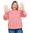 © Krakenimages.com - Hispanic woman with pink hair wearing casual winter sweater showing and pointing up with fingers number ten while smiling confident and happy.