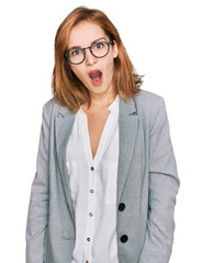 Poster - Young caucasian woman wearing business style and glasses in shock face, looking skeptical and sarcastic, surprised with open mouth