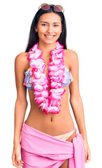 Poster - Young beautiful latin girl wearing bikini and hawaiian lei looking positive and happy standing and smiling with a confident smile showing teeth