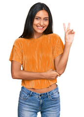 Wall Mural - Young brunette arab woman wearing casual clothes smiling with happy face winking at the camera doing victory sign. number two.