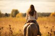 Young girl goes sorrel horse riding in field, back view