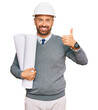 © Krakenimages.com - Handsome middle age man holding paper blueprints smiling happy and positive, thumb up doing excellent and approval sign