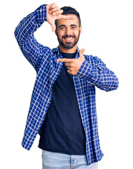 Wall Mural - Young hispanic man wearing casual clothes smiling making frame with hands and fingers with happy face. creativity and photography concept.