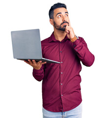 Sticker - Young hispanic man holding laptop serious face thinking about question with hand on chin, thoughtful about confusing idea